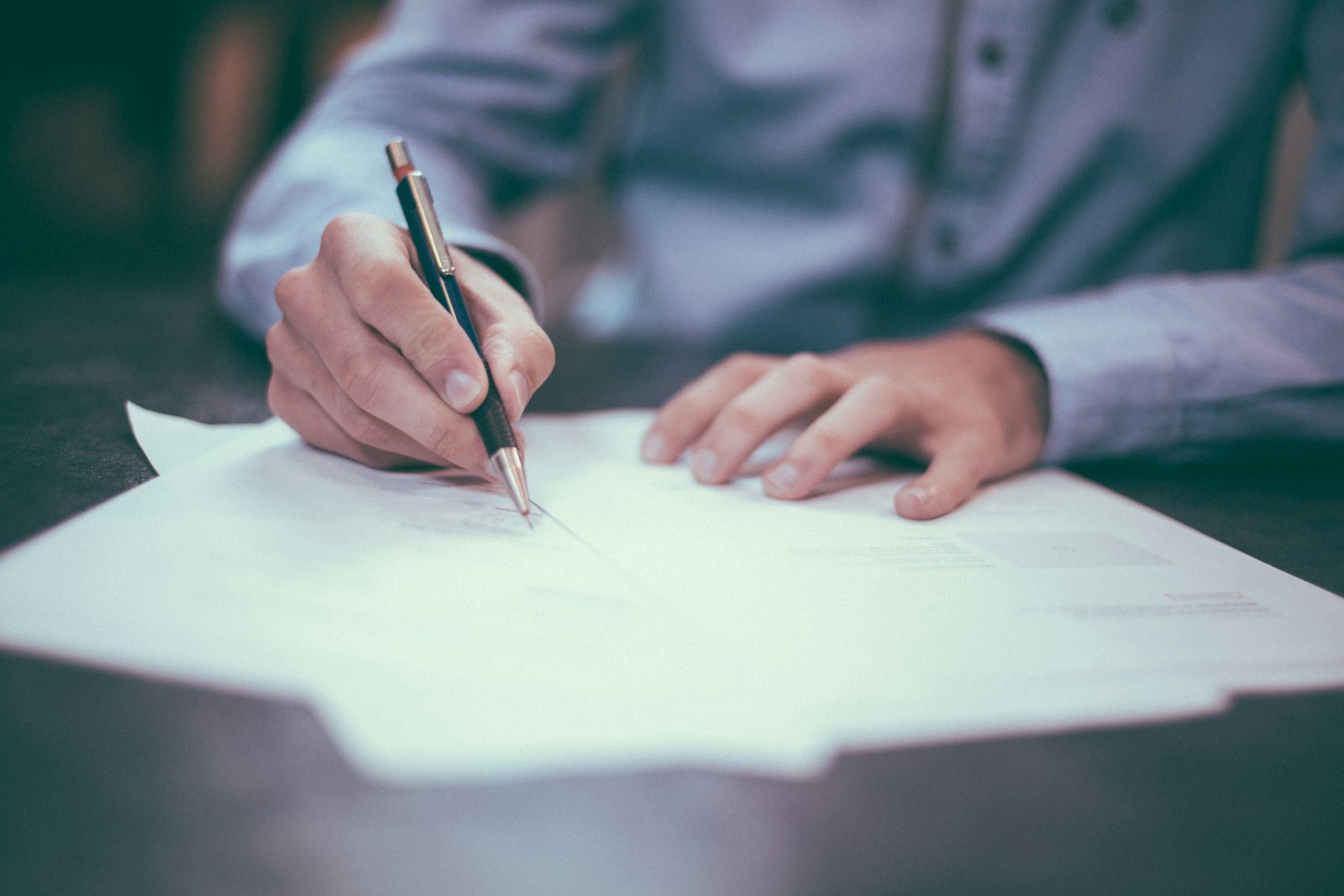 A person signing a document with a pen